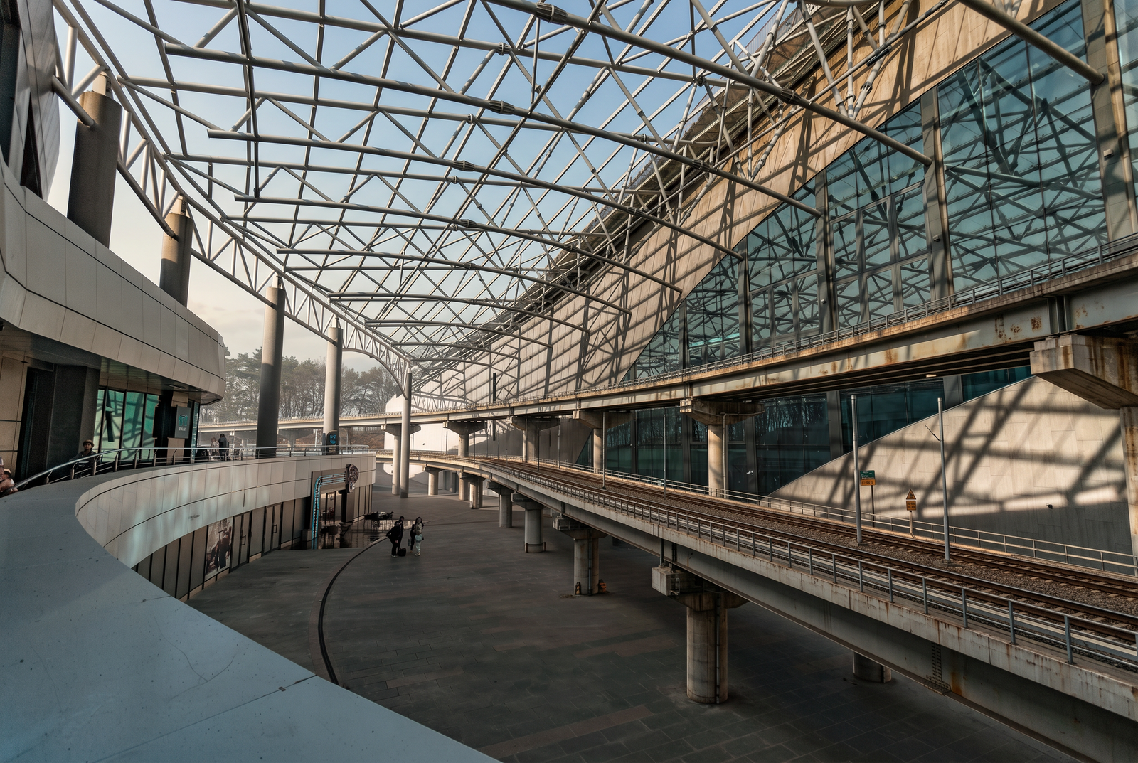 Steel-framed transit station with expansive truss canopy over elevated rail platforms